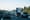 Trucks and passenger vehicles sharing a highway with trees and mountains in the background.