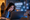 Young girl using a laptop with AI chatbot and data privacy icons on screen, while a concerned parent watches from the doorway.