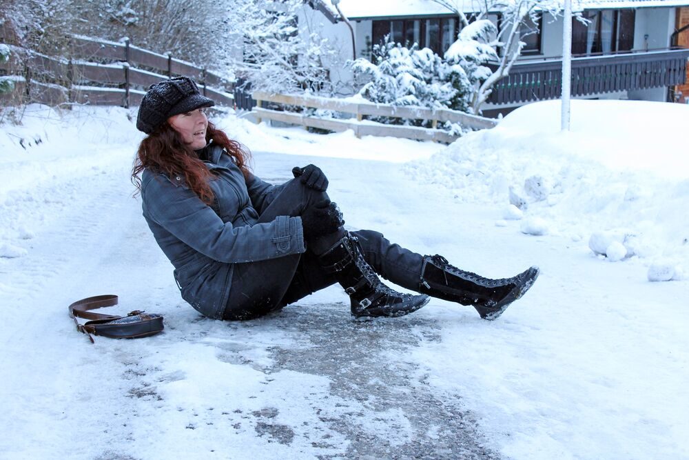 A woman holds her knee in pain after falling on an icy walkway