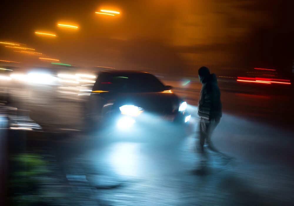 A car bearing down on a hard-to-see pedestrian crossing the street at night