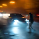 A car bearing down on a hard-to-see pedestrian crossing the street at night