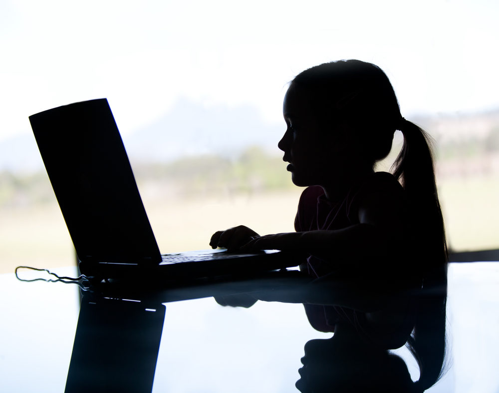 Silhouette of young girl on laptop at desk.