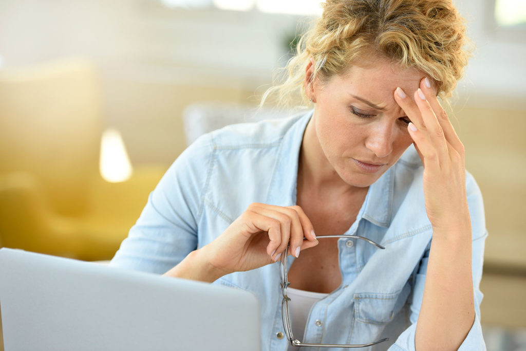 A woman using a laptop rests her head on her hand