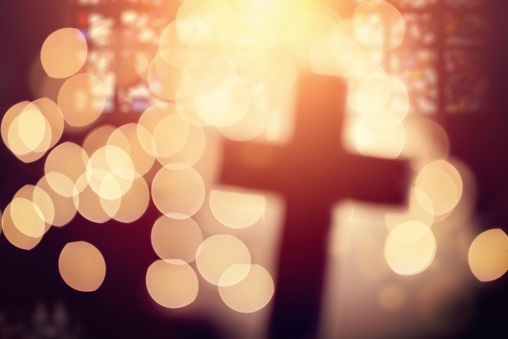 Abstract defocussed cross silhouette in church interior against stained glass window