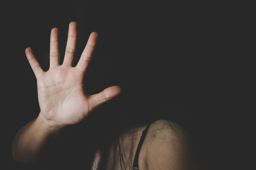 woman holding up her hand against an abuser with black background.