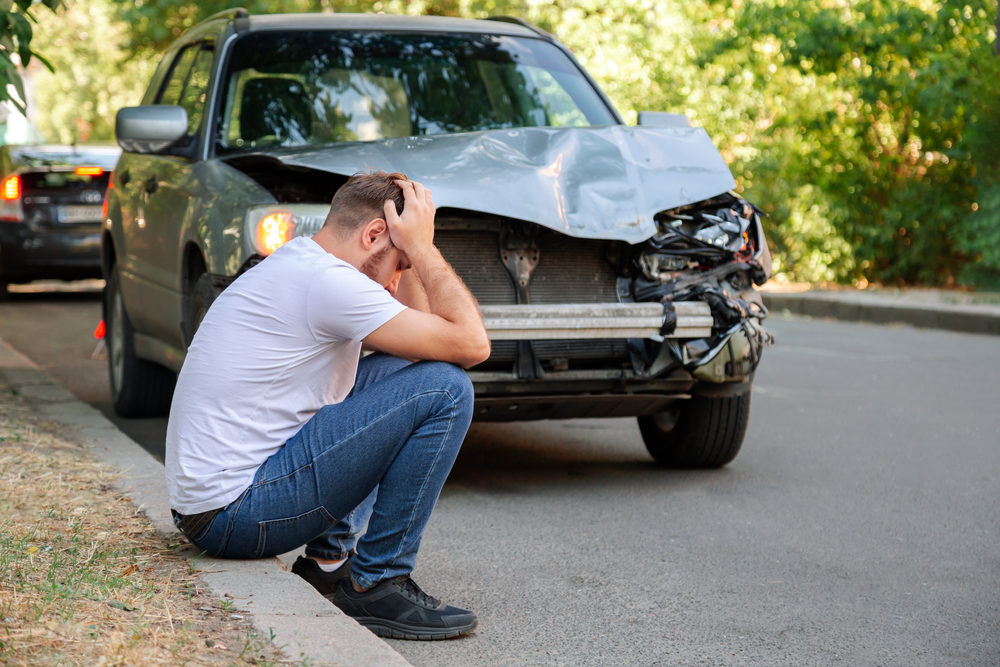 Man holding his head sitting in front of his car after a car accident.