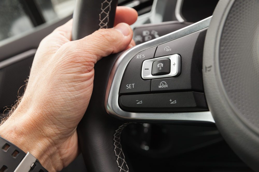 Adaptive cruise control panel buttons on modern car steering wheel, interior details with driver hand