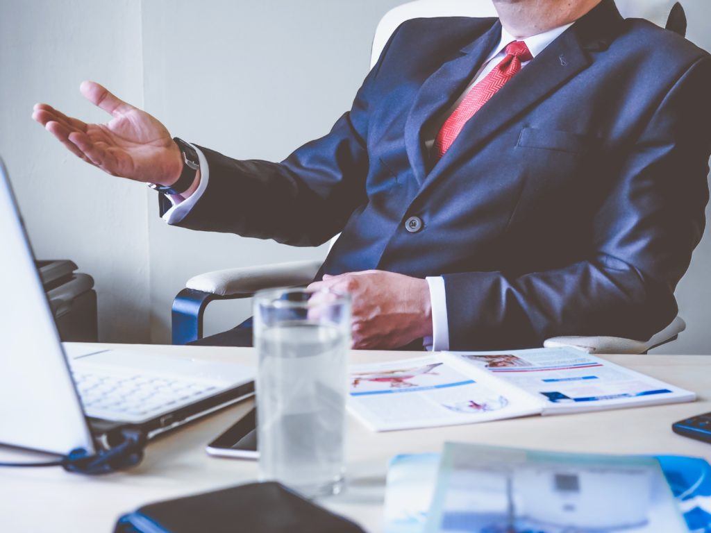 Why Is My Detroit Lawyer Not Responding To Me About My Car Accident Case? A man in a suit discusses something at a desk covered in a laptop and paperwork