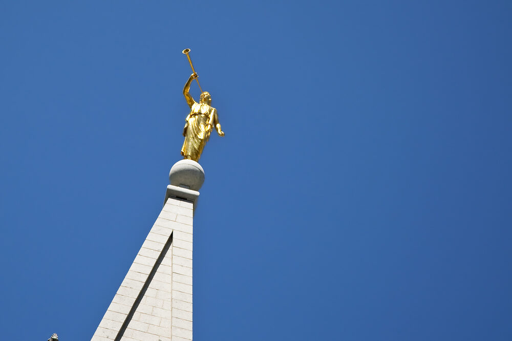 a view of angel moroni on top of a jesus christ of latter-day saints mormon temple with blue sky behind