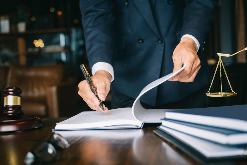 male attorney holding a pen going through a contract at desk with gavel and scales