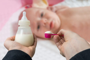 hands holding a bottle and formula to feed baby in blurred background