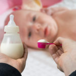 hands holding a bottle and formula to feed baby in blurred background