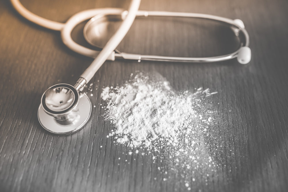 Baby talcum powder spilled on wooden table near stethoscope 