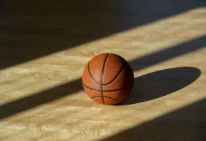 Basketball on hardwood court floor with natural lighting.
