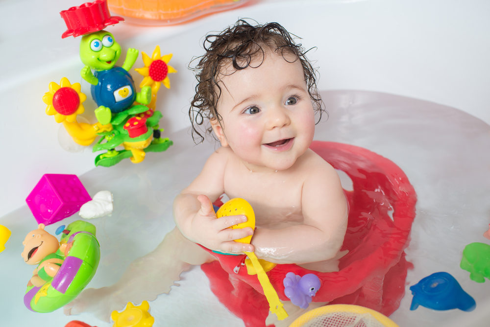baby sitting in water in a bath and playing with toys.