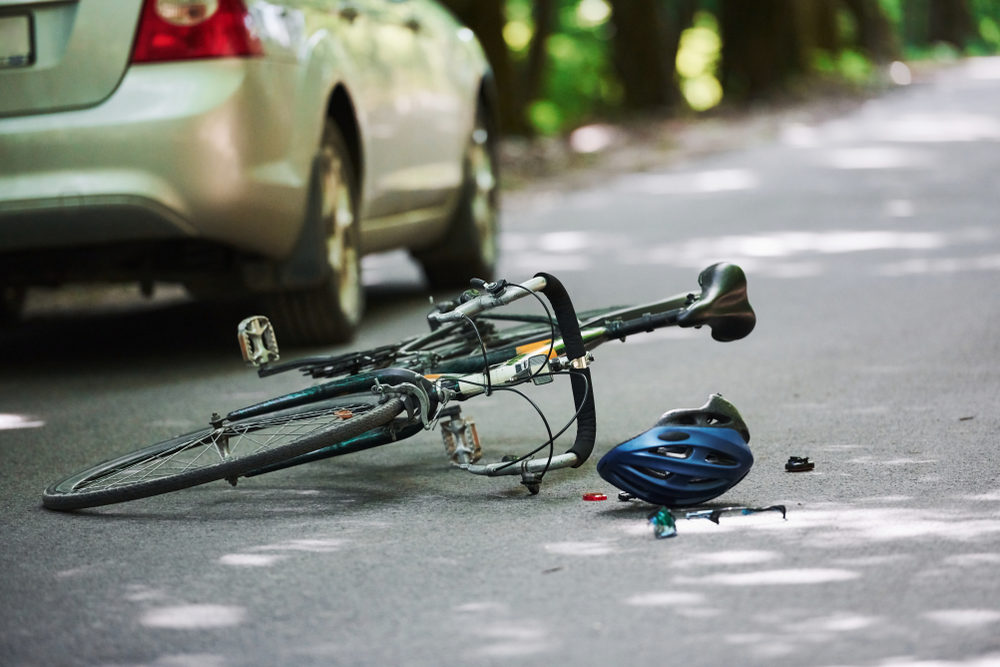 Bicycle and silver colored car accident on the road at forest at daytime.