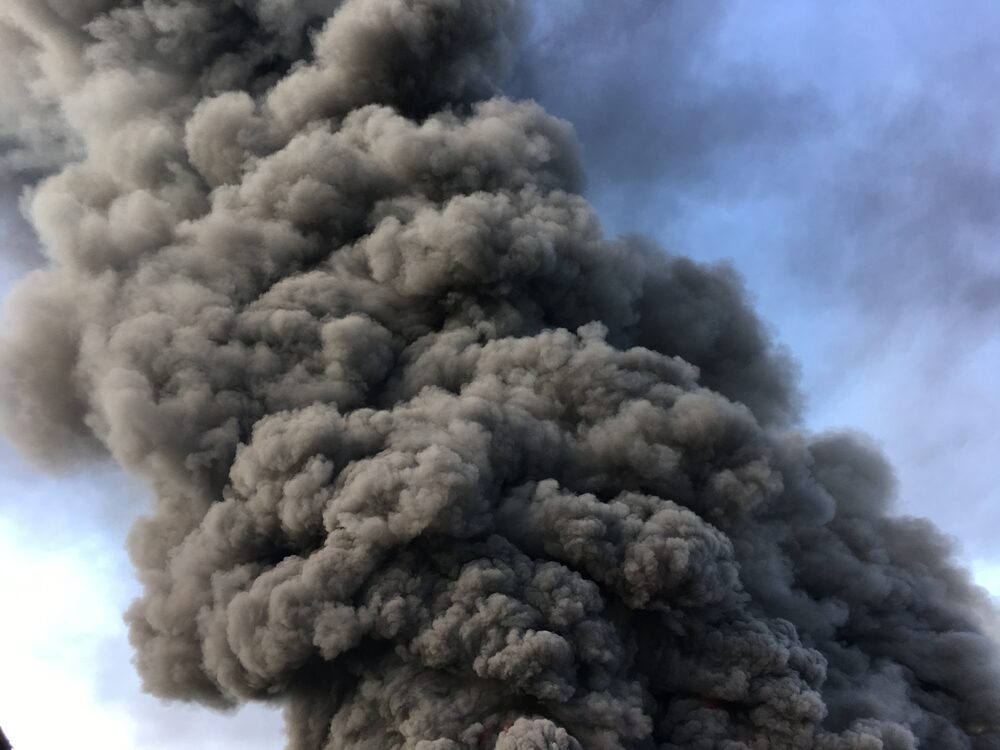 Warehouse engulfed in raging fire with huge column of smoke
