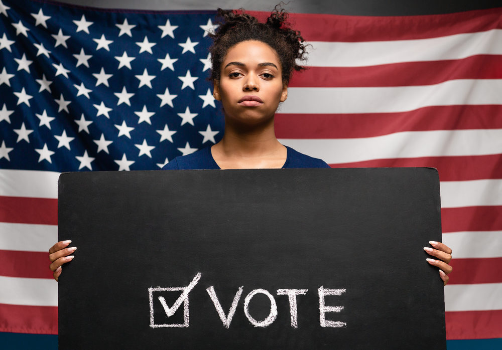 Black woman holding Vote sign against american flag