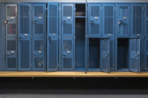 Blue metal cage lockers with a wood bench in a locker room with some doors open and some doors closed