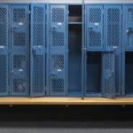 Blue metal cage lockers with a wood bench in a locker room with some doors open and some doors closed