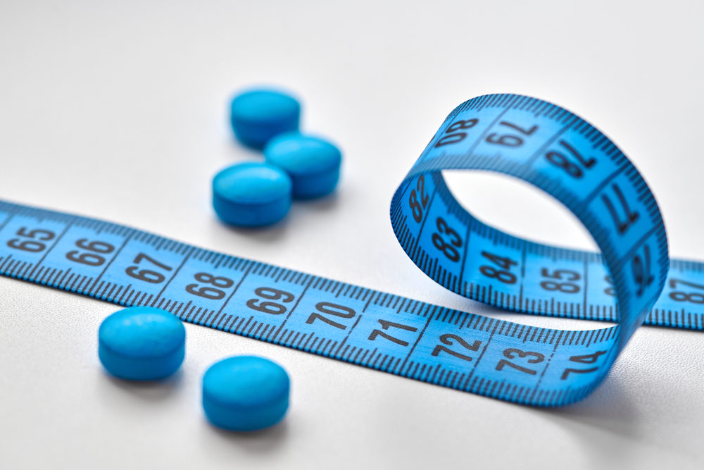 Blue round diet pills and measuring centimeter tape isolated on white background.