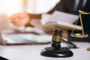 selected focus on a gavel at attorney's desk with blurred layer at laptop behind