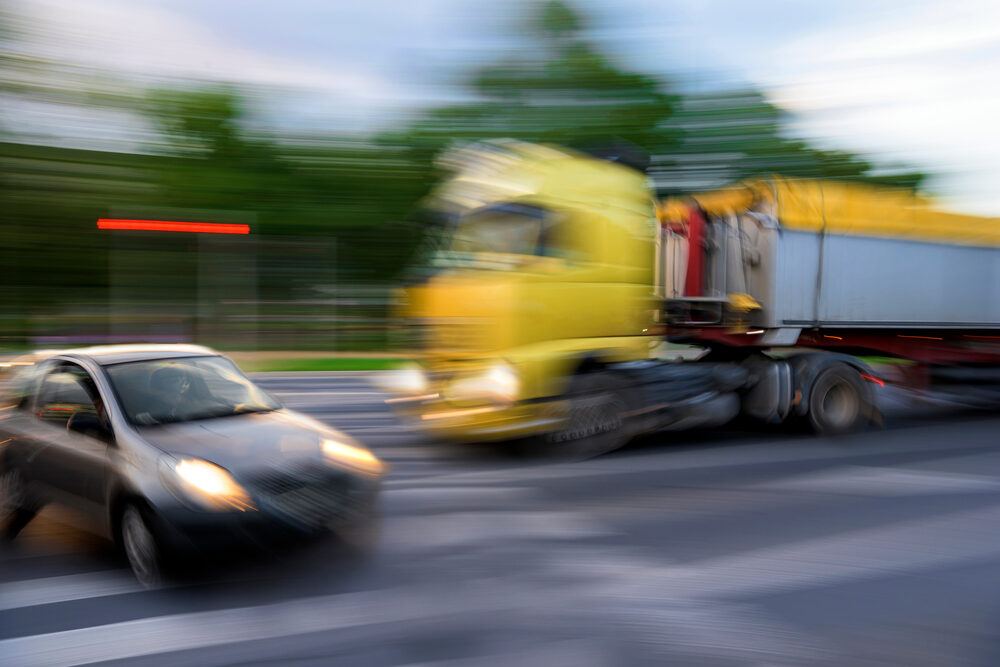 Who is liable for a truck crash in Detroit? Dangerous traffic situation between a car and a truck in motion blur.
