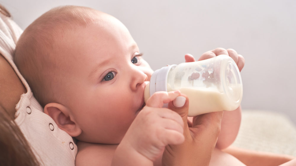 Mom feeds her child baby milk powder in a baby bottle