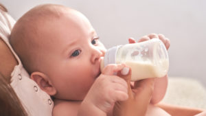 Mom feeds her child baby milk powder in a baby bottle