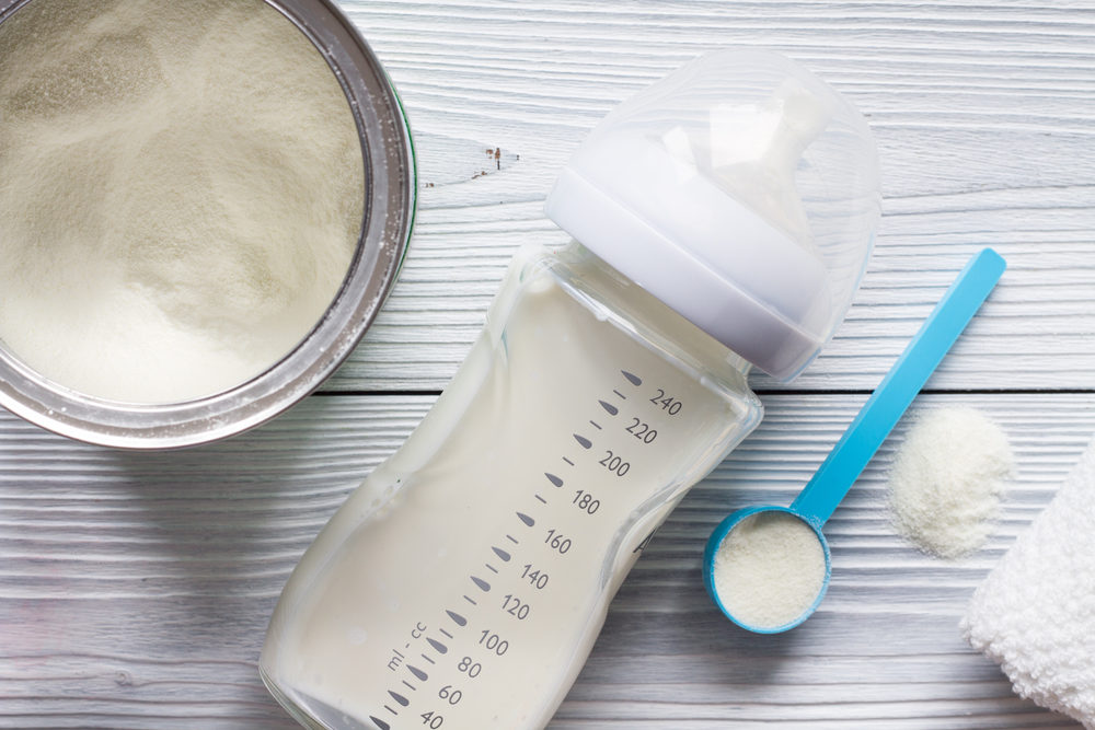 Milk powder for baby in bottle and measuring spoon on table