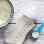 Milk powder for baby in bottle and measuring spoon on table
