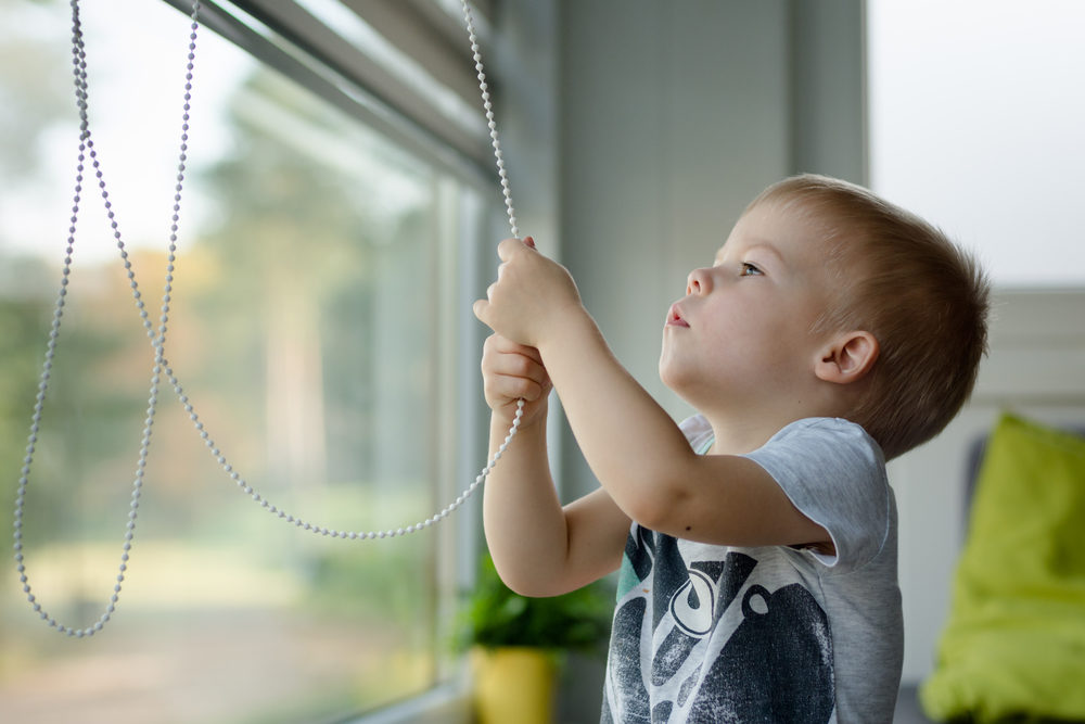 Little, three years old boy he raises the blinds in the windows and looking out the window