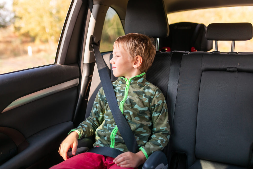 Little boy sitting on a booster seat buckled up in the car.