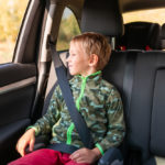Little boy sitting on a booster seat buckled up in the car.