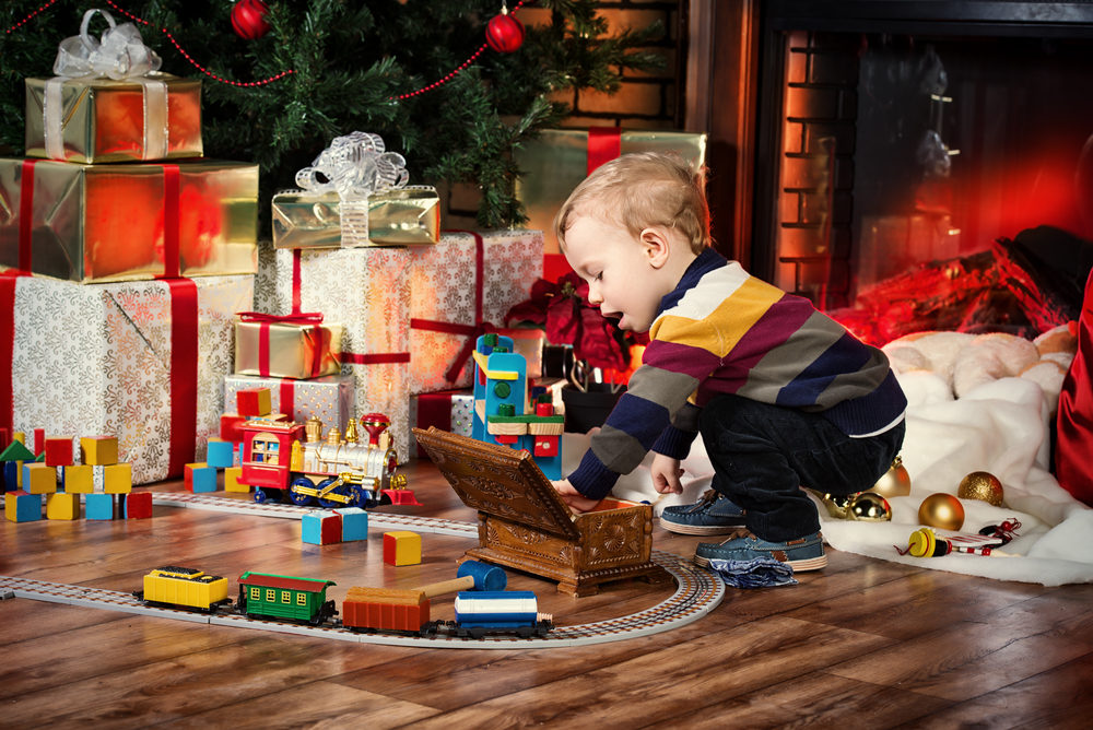 Little boy playing with toys at home near the fireplace and Christmas tree.