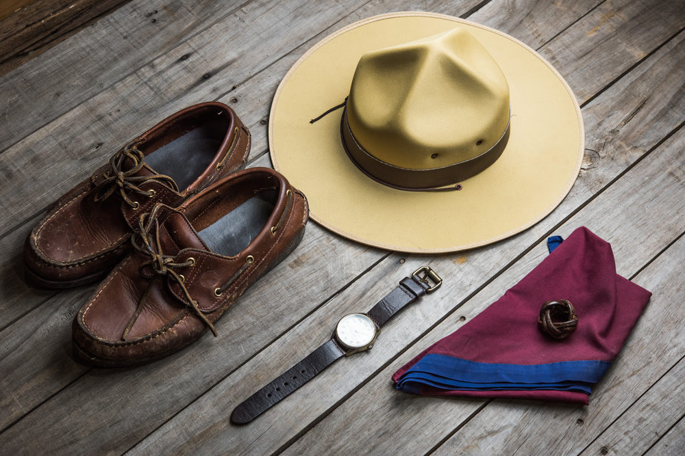 Parts of a scout leader uniform layed out on a floor: shoes, hat, watch, scarf