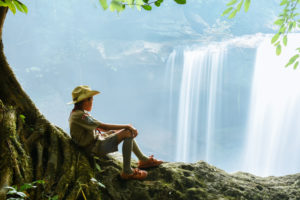Alone boy scout sitting on tree near waterfall