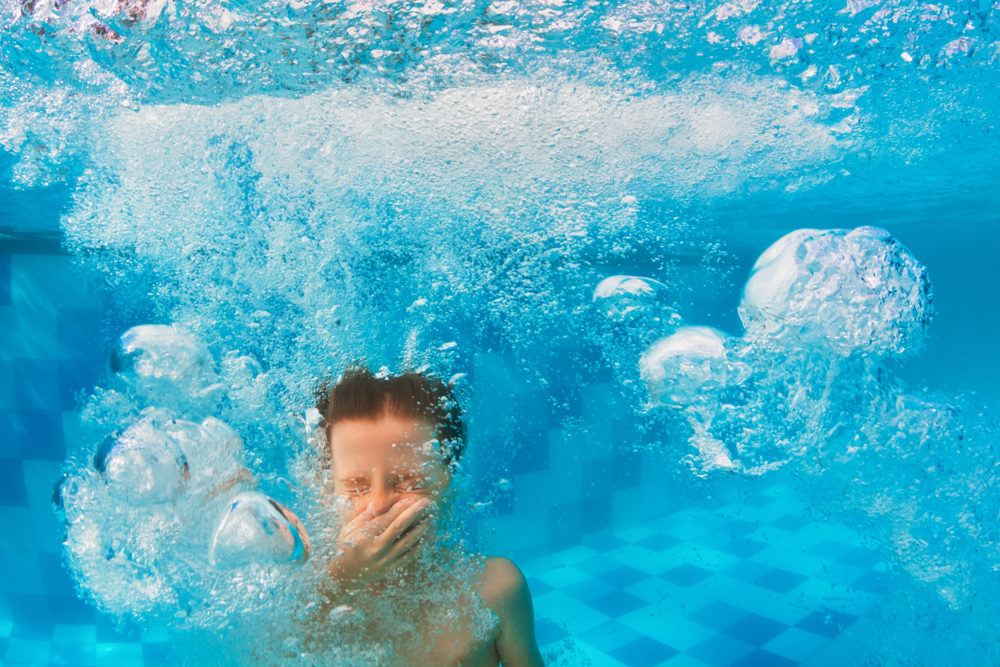 A boy plugs his nose while under water in a pool