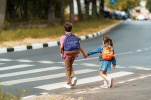 brother and sister holding hands about to use a pedestrian crosswalk on the way to school