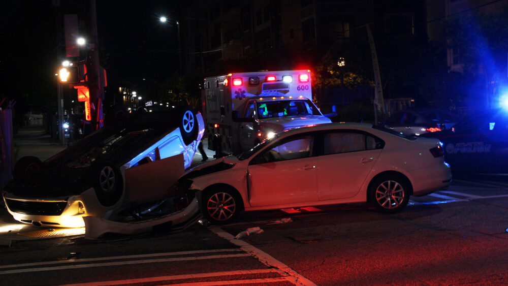 car accident scene at night with an overturned white car crashed into another white car with ambulance on site