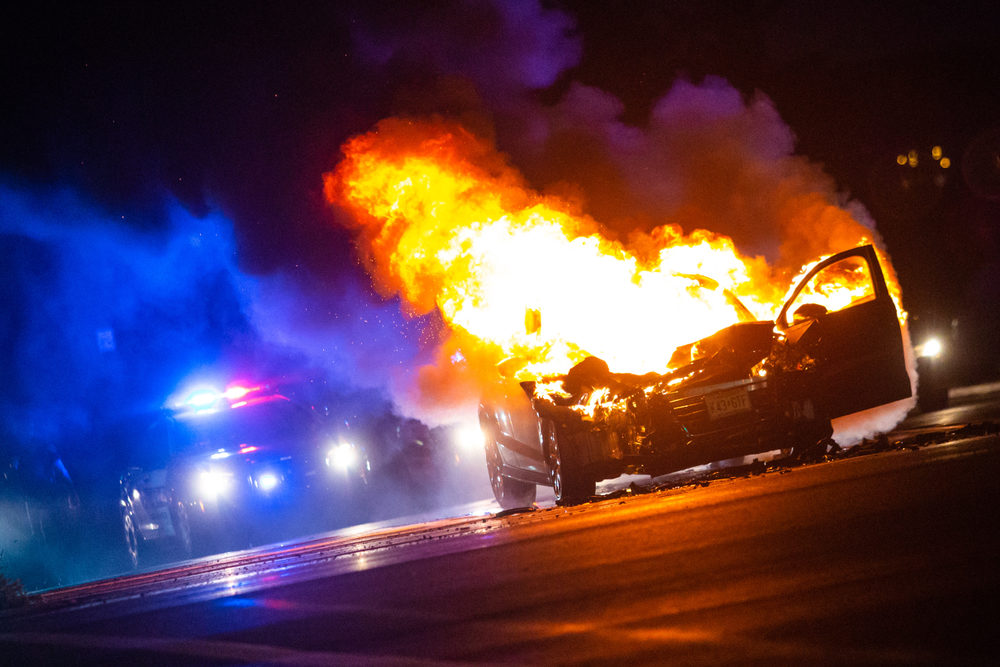 car on fire at night with police lights in background