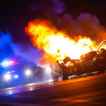 car on fire at night with police lights in background