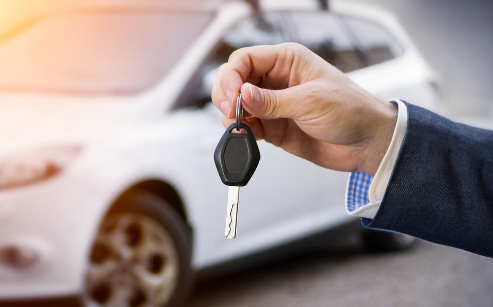 Male holding car keys with car on background