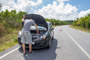 Man looking under the hood of his car that is broke down on the roadway