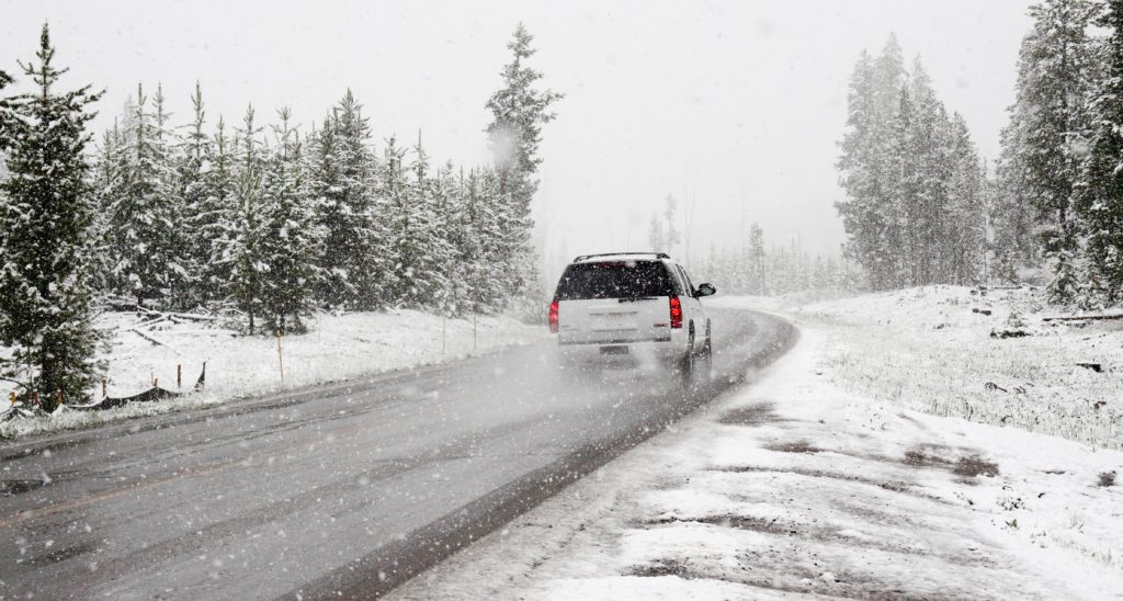A white SUV drives through a curce on a wet, snowy road