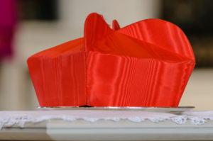 A cardinal's Beretta hat sits on a table during a requiem mass