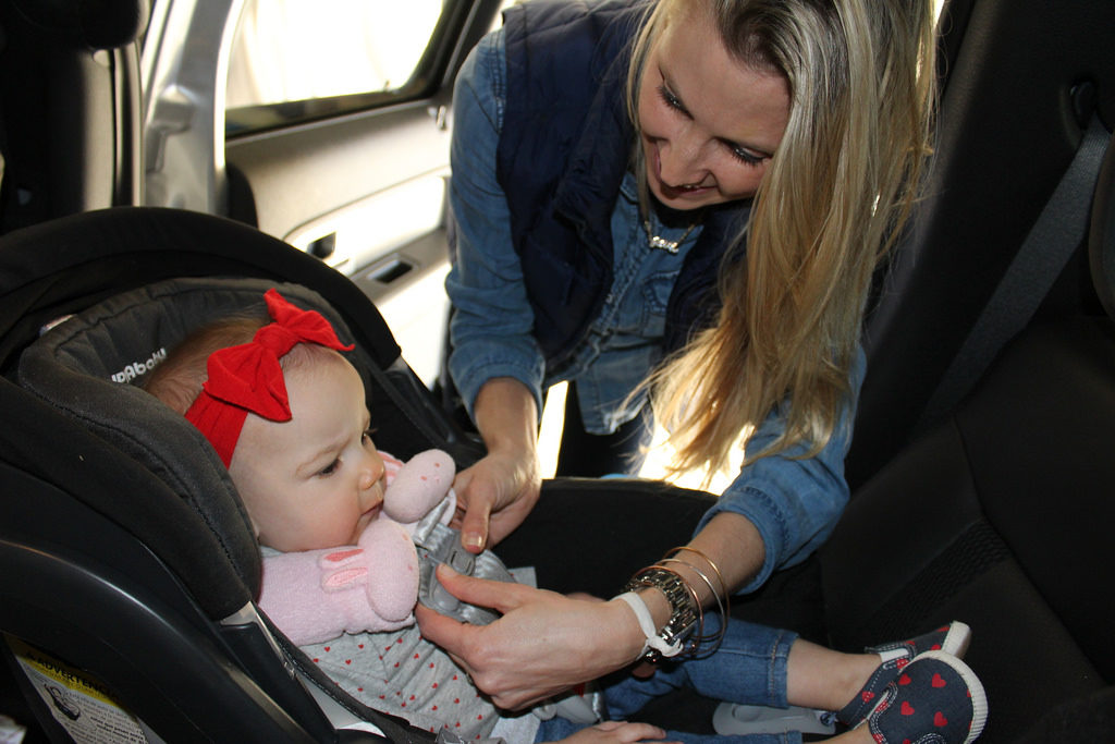 A young mother straps an infant girl into a rear-facing car seat