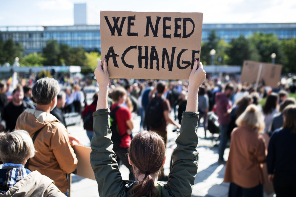 female protester holding a sign that says we need a change among a crowd of activists