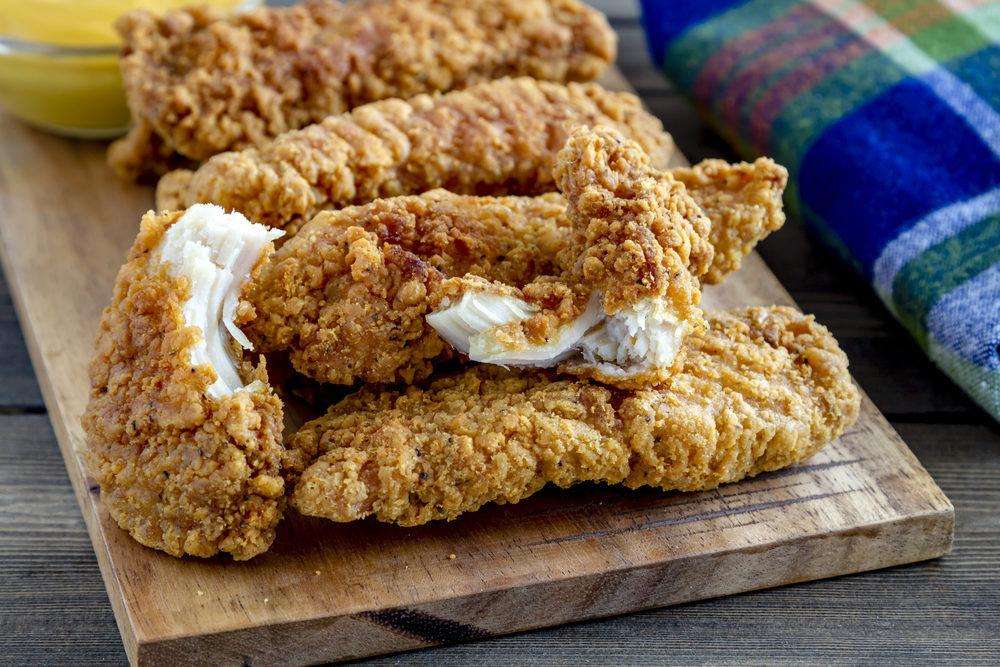 Close up of chicken fingers on wooden cutting board with homemade honey mustard dipping sauce