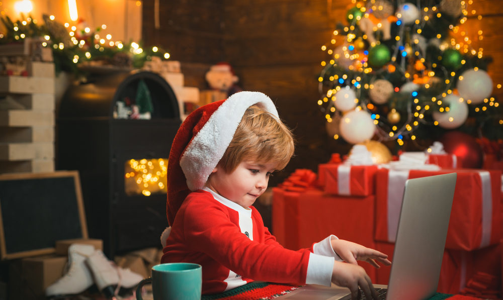 On GivingTuesday, Here Are 3 Civil Justice Organizations to Know About . Happy little smiling boy wearing Santa clothes and writing a letter on his laptop.